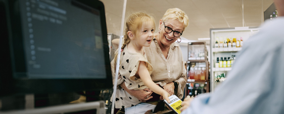 Dame mit Kind auf dem Arm an der Supermarktkasse beim Geld abheben